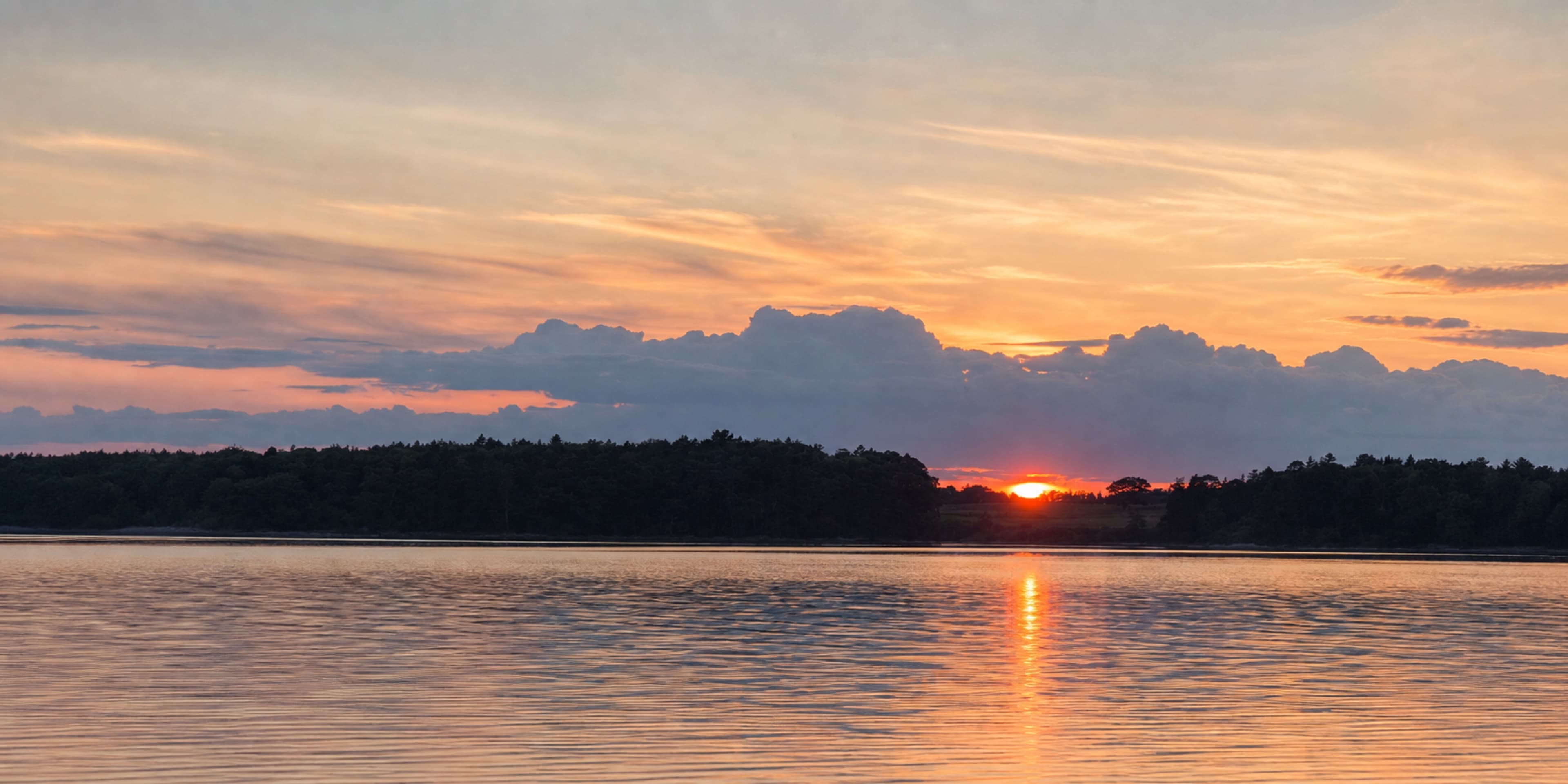 Sunset over calm water and a tree-lined shore